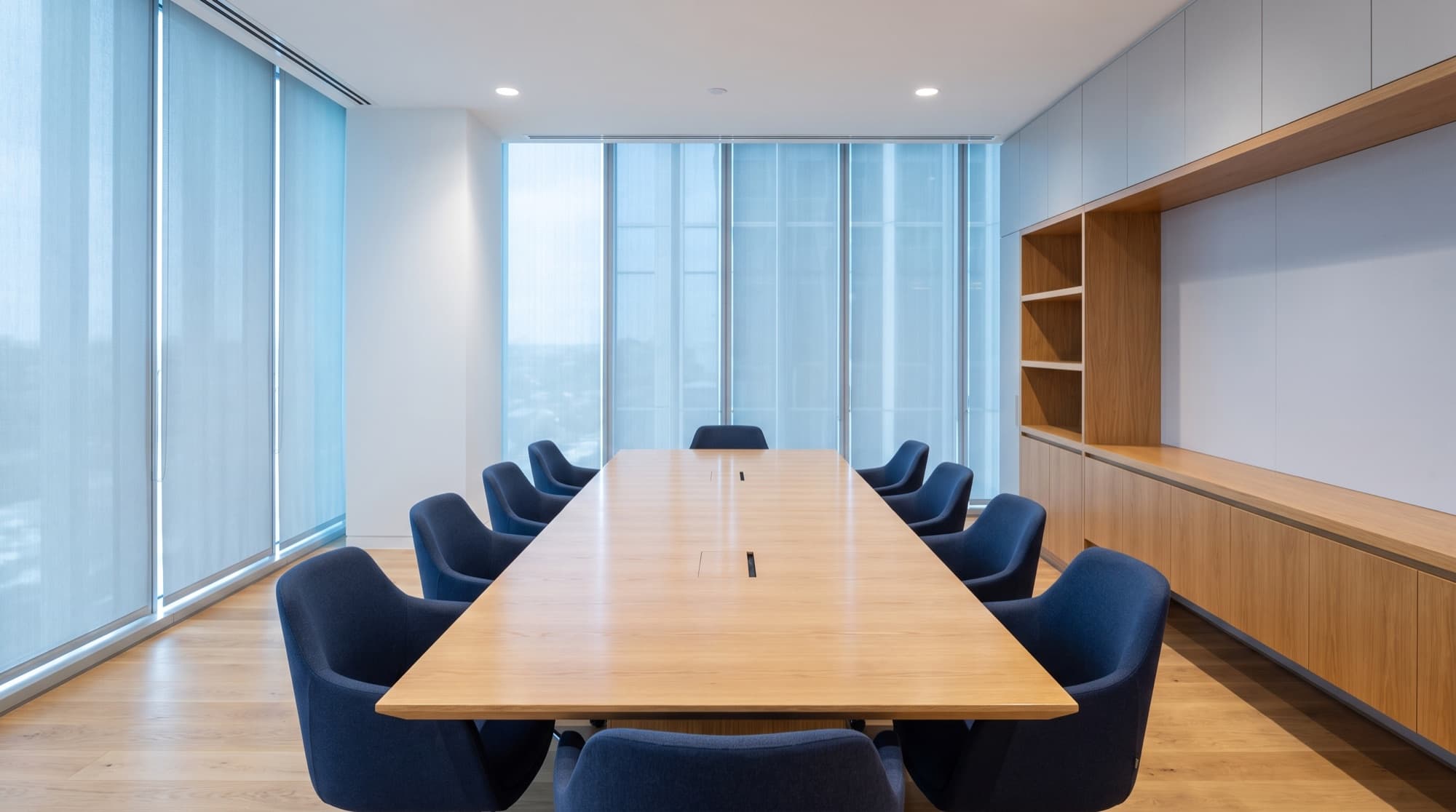 A bright, modern office meeting room with navy chairs and an oak table